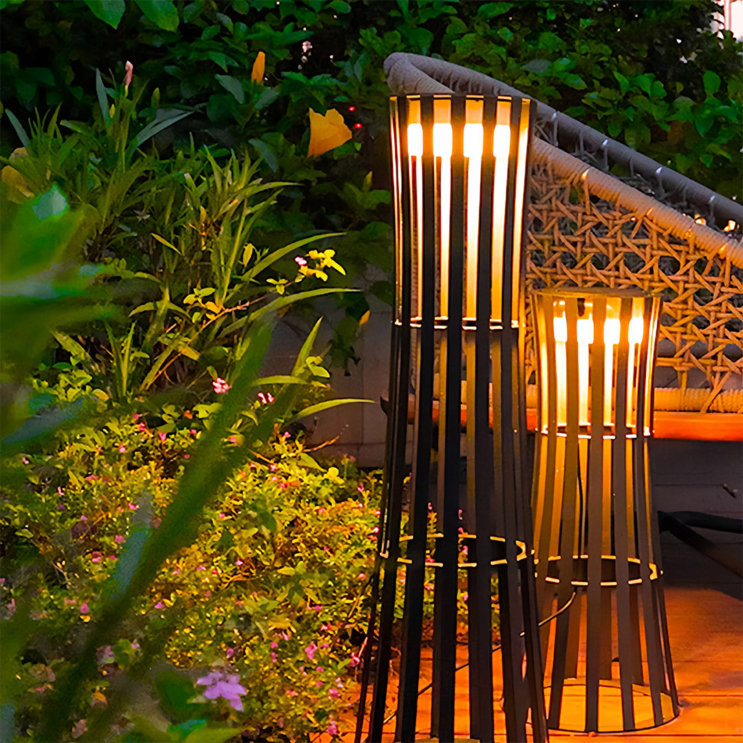 Pair of woven rattan-style outdoor black lanterns suspended from a wooden patio roof, providing warm, decorative light near a glass door.