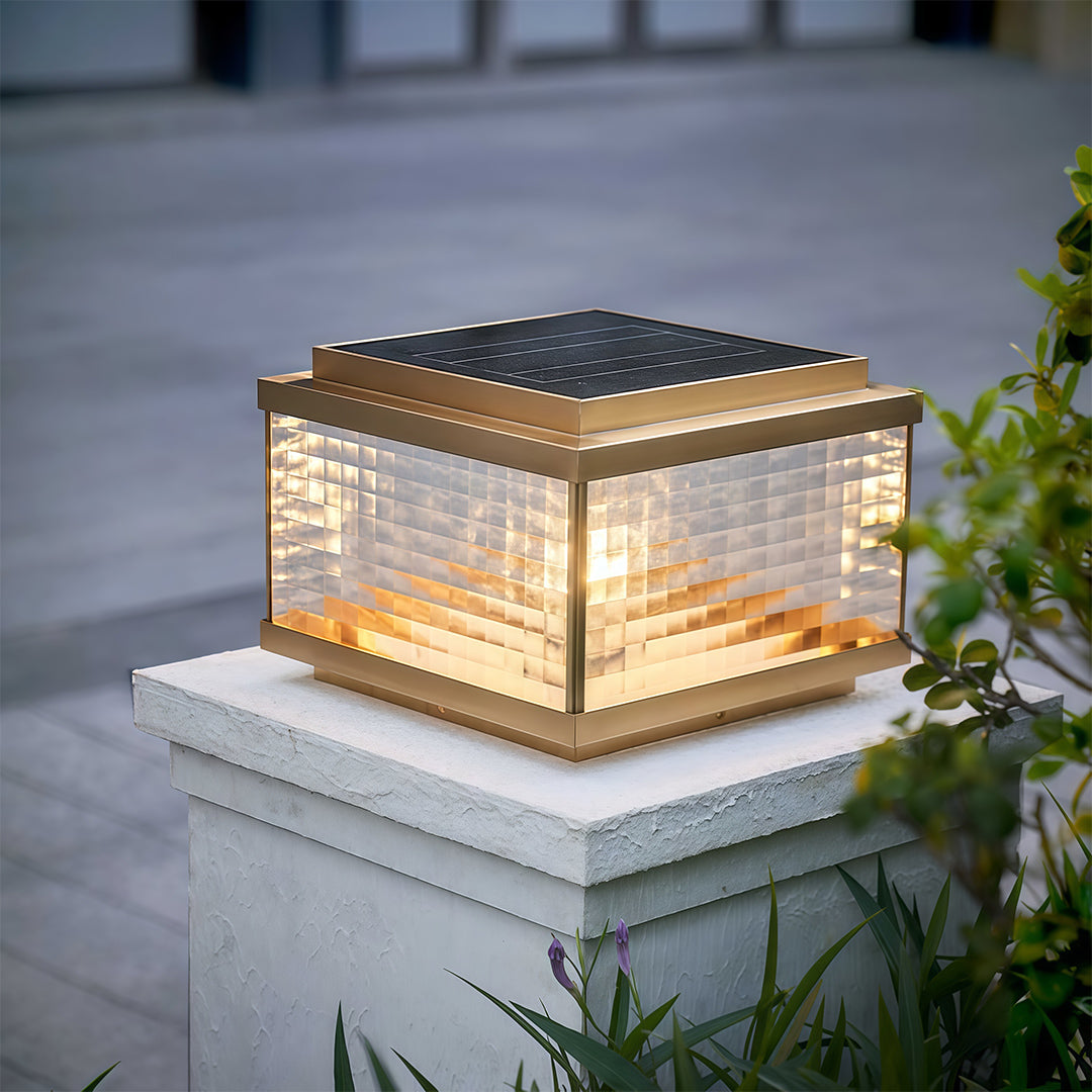 Pillar cap light on concrete post illuminating paved outdoor pathway with warm evening glow.