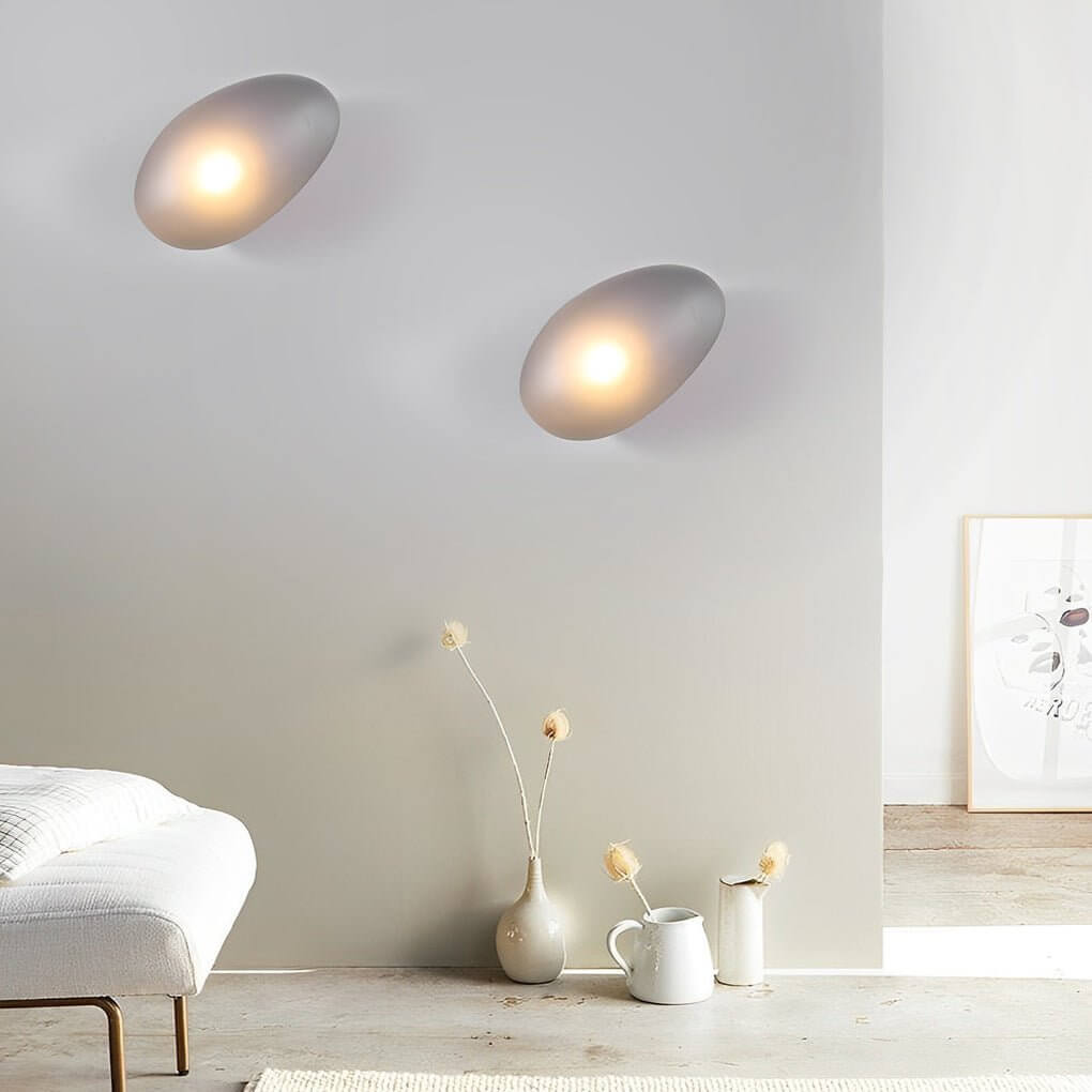 Pebbles wall lamp casting a gentle light in a contemporary living room with a gray sofa.