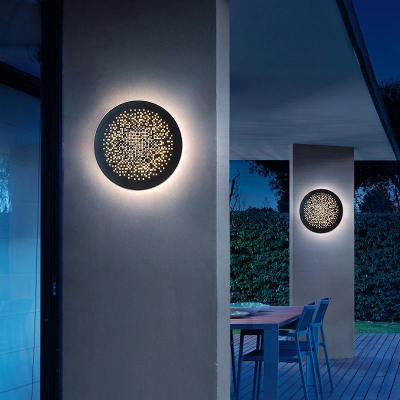 Perforated metal wall sconce creating ambient lighting on a modern outdoor wall at night.