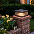 Outdoor pillar mount light placed on a brick column, casting soft light around landscaping and pathway edges at night.