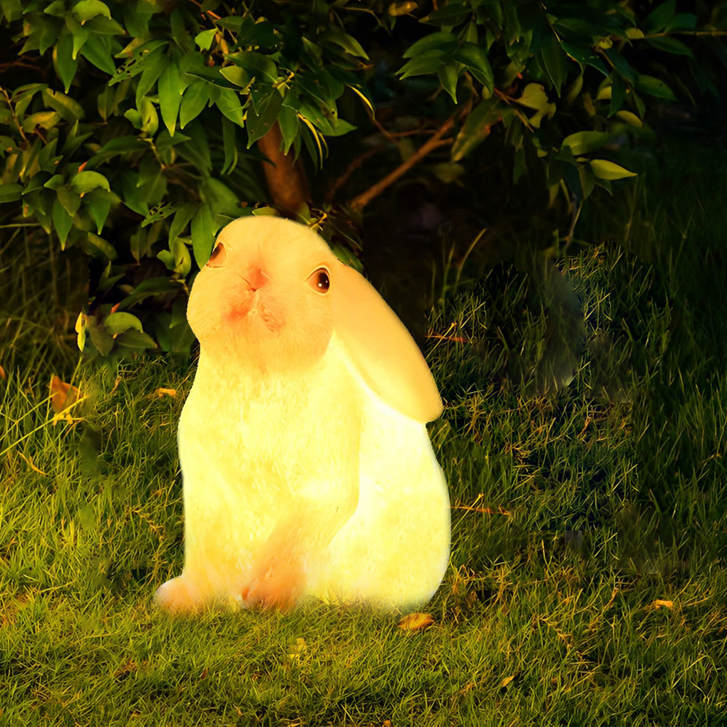 Rabbit garden light holding a carrot, casting a soft light in a dark garden setting.