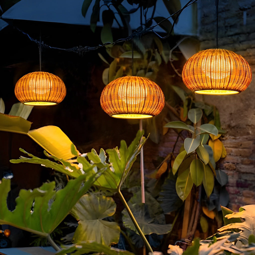 Rattan outdoor pendant light hanging above lush green plants, creating a natural ambiance.