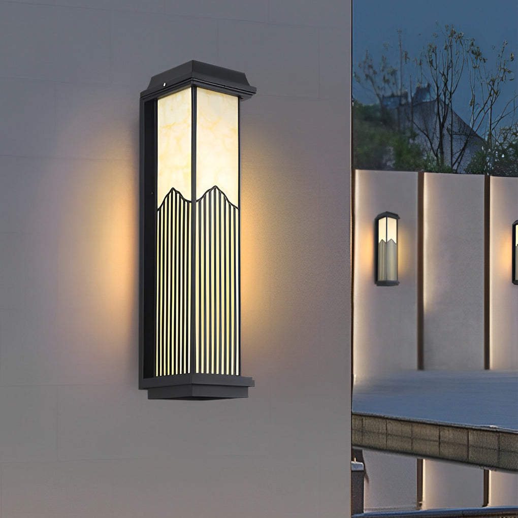 Rectangular outdoor sconce with a black finish, providing ambient light near a garden.