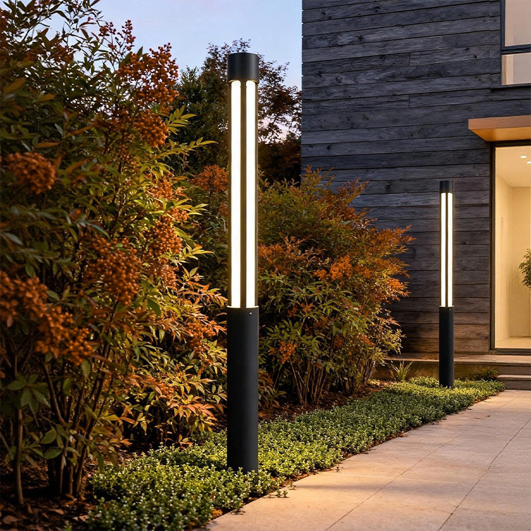 Residential bollard lights lining a modern garden walkway, featuring tall black posts with vertical diffused light for outdoor pathways.