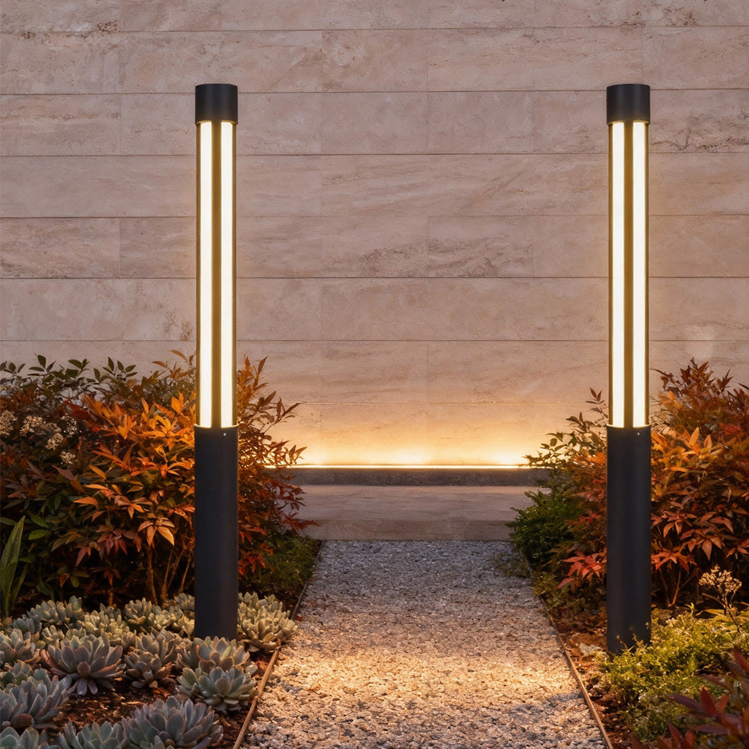 Residential bollard lights installed beside a gravel path and plants, showing slim vertical light columns for contemporary outdoor lighting design.