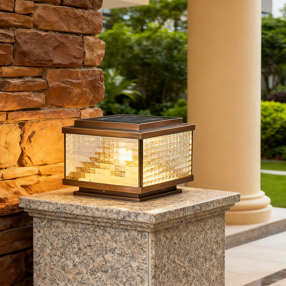 Pillar cap lights on brick stone posts framing residential driveway entrance with natural foliage backdrop.