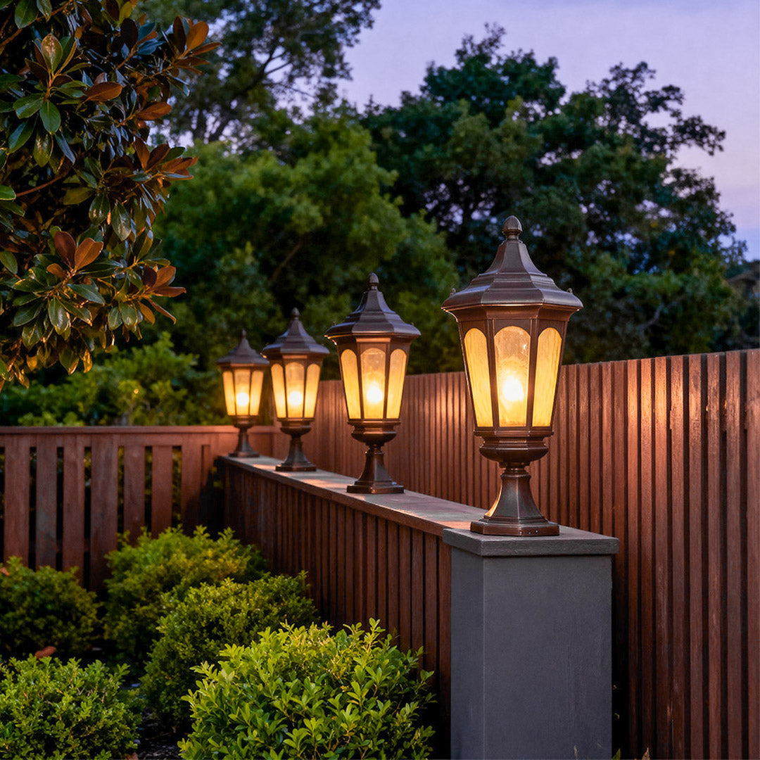 Multiple residential pillar light glowing warmly on grey pillars along wooden fence at twilight