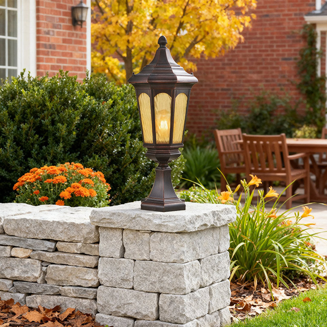 Residential pillar light illuminating stone wall entrance with orange mums and outdoor furniture backdrop