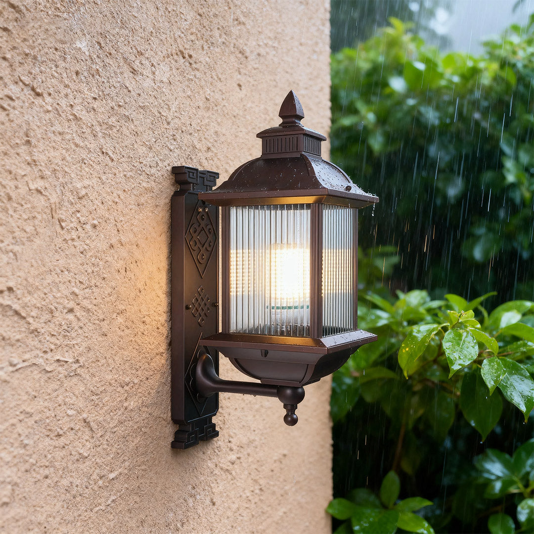 Single retro outdoor wall light glowing warmly on rough stucco surface with garden view