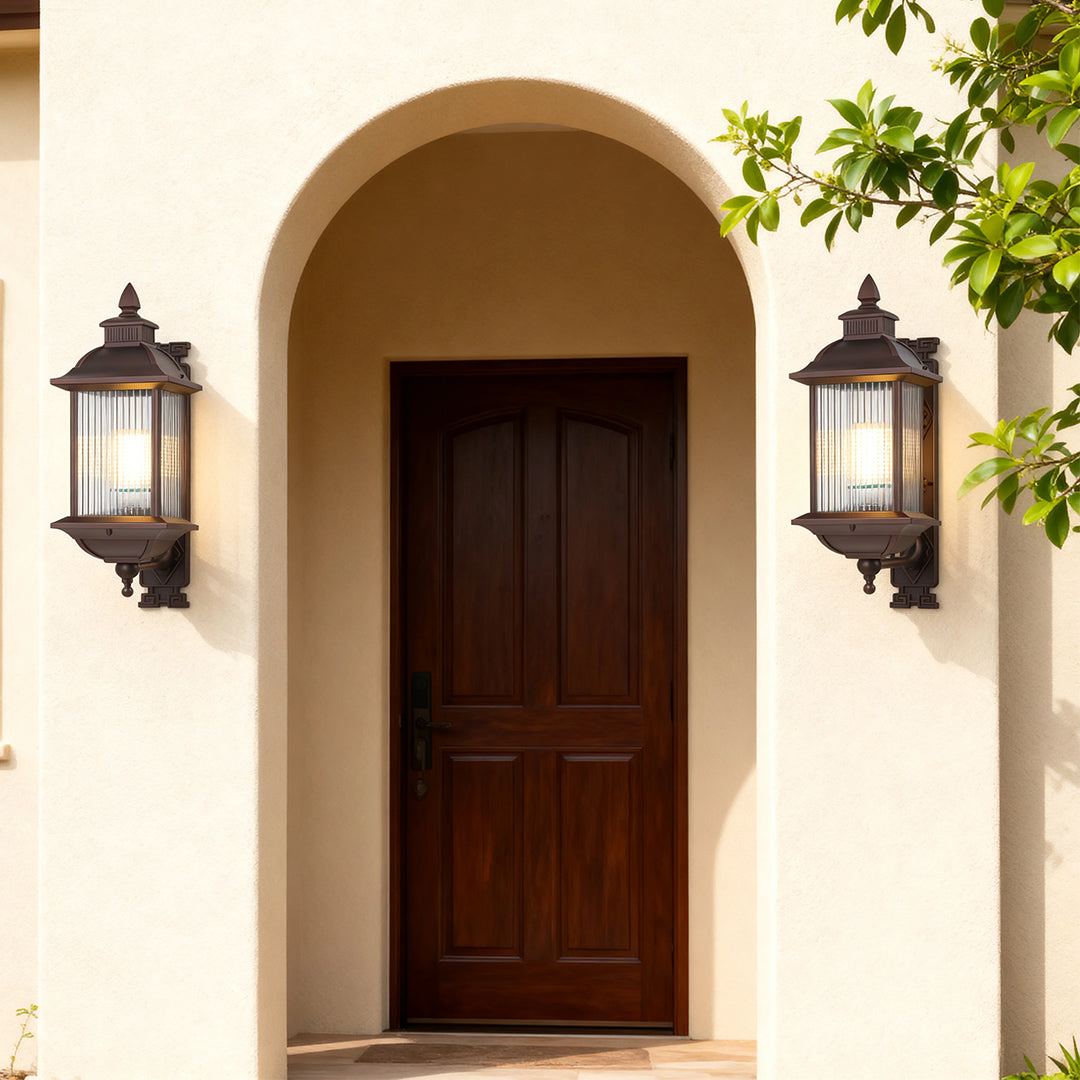 Matching retro outdoor wall lights framing arched wooden doorway on cream-colored Mediterranean facade