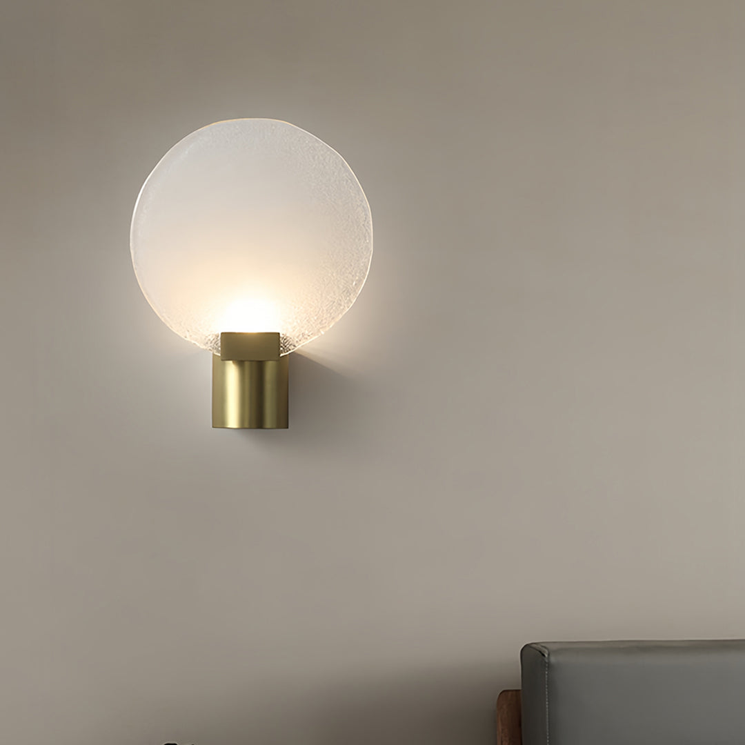 Round wall light with a frosted glass shade and gold base, mounted beside a window with sheer curtains.