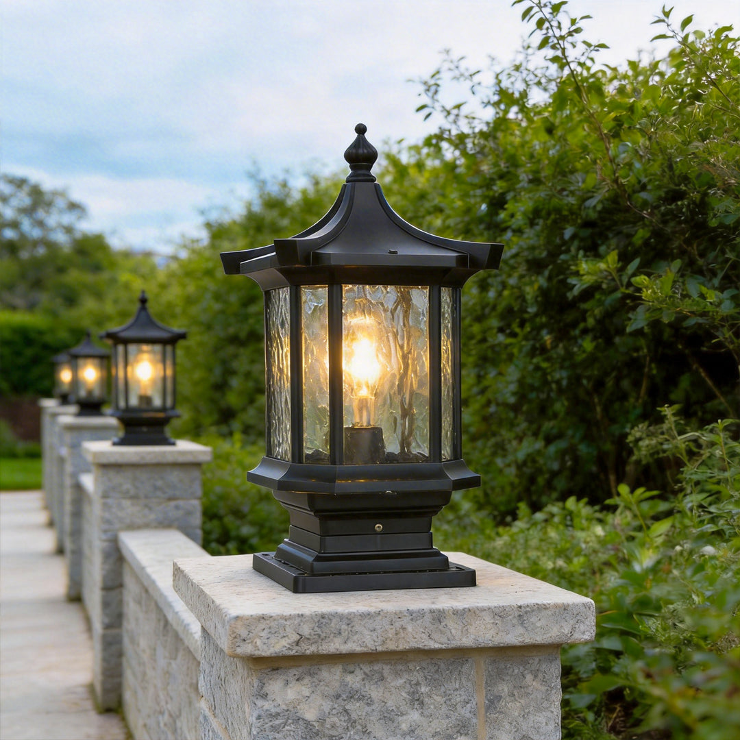 Row of black lantern pillar lights illuminating a stone garden boundary wall pathway perfectly.