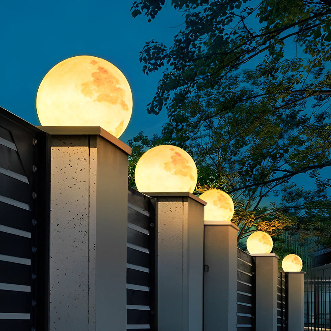 Row of glowing moon-shaped stone pillar lights installed on a dark metal fence in the evening.