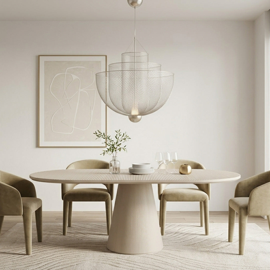 Silver mesh tiered chandelier hanging over a light cream dining table with beige velvet chairs.
