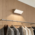 Modern silver wall lights above a wooden clothing rack creating warm ambient lighting in a luxury boutique interior.
