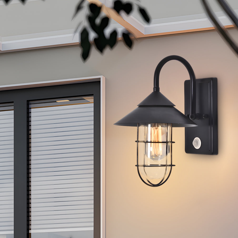 Sleek barn wall light with curved arm and clear glass, installed on a white house exterior wall.