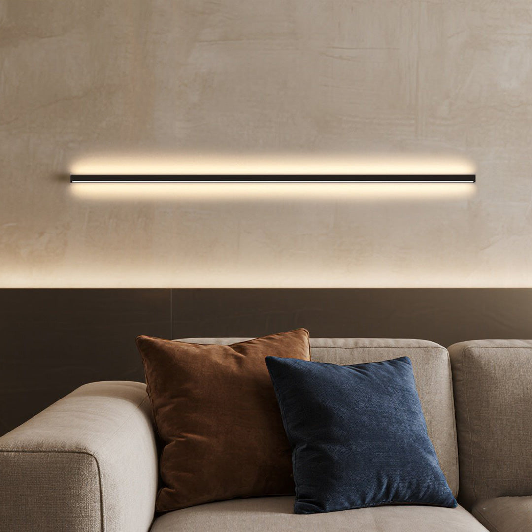Modern linear wall sconce with sleek horizontal LED light, mounted above sofa for warm and minimalist indoor illumination.