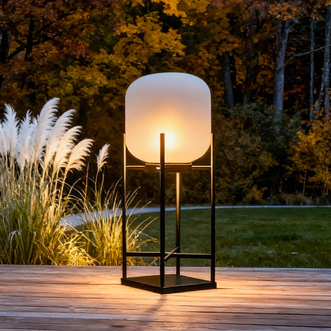 Outdoor standing light casting soft glow on patio with comfortable cushioned chairs and potted plants.