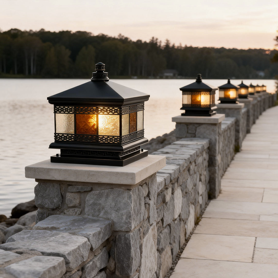 Solar column pillar lights aligned along a lakeside stone wall, creating an elegant pathway lighting effect at dusk.
