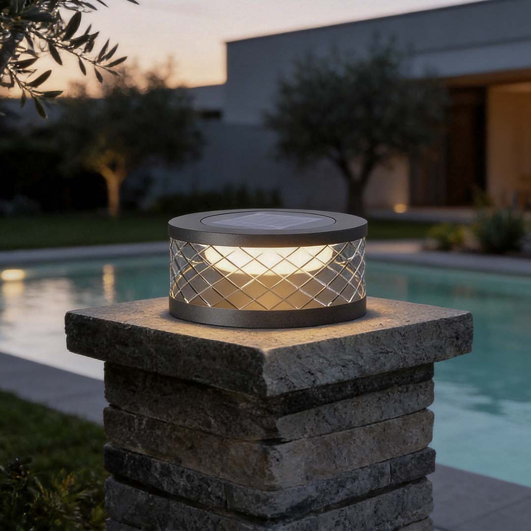 Solar cylinder pillar light with a geometric pattern, illuminating a poolside area at dusk.