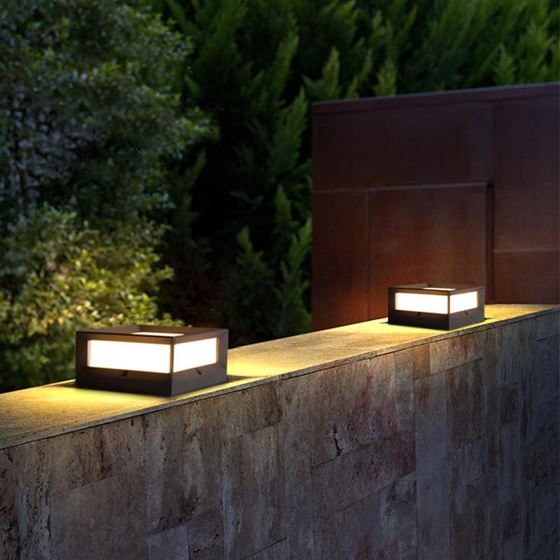 Solar garden pillar lights with black frame, mounted on stone pillars near greenery.