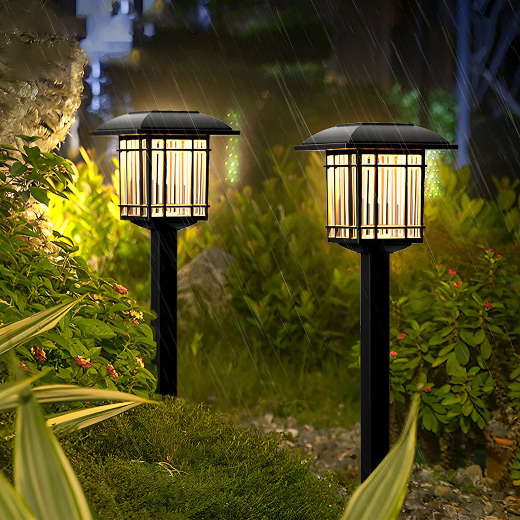 Solar outdoor lawn light with a black finish, glowing warmly in a lush garden setting.