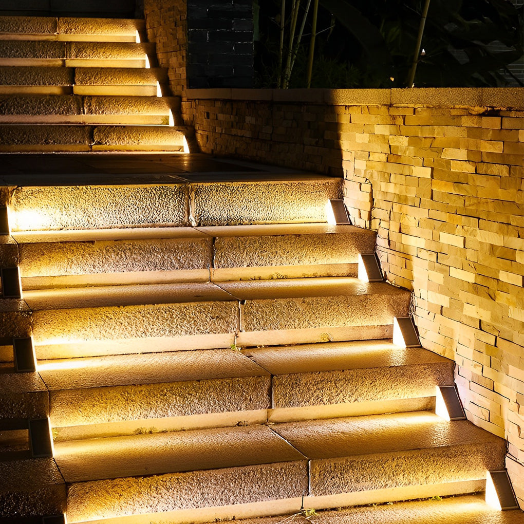 Solar powered lights for steps casting bright warm light on outdoor stair risers beside a stone wall at night.