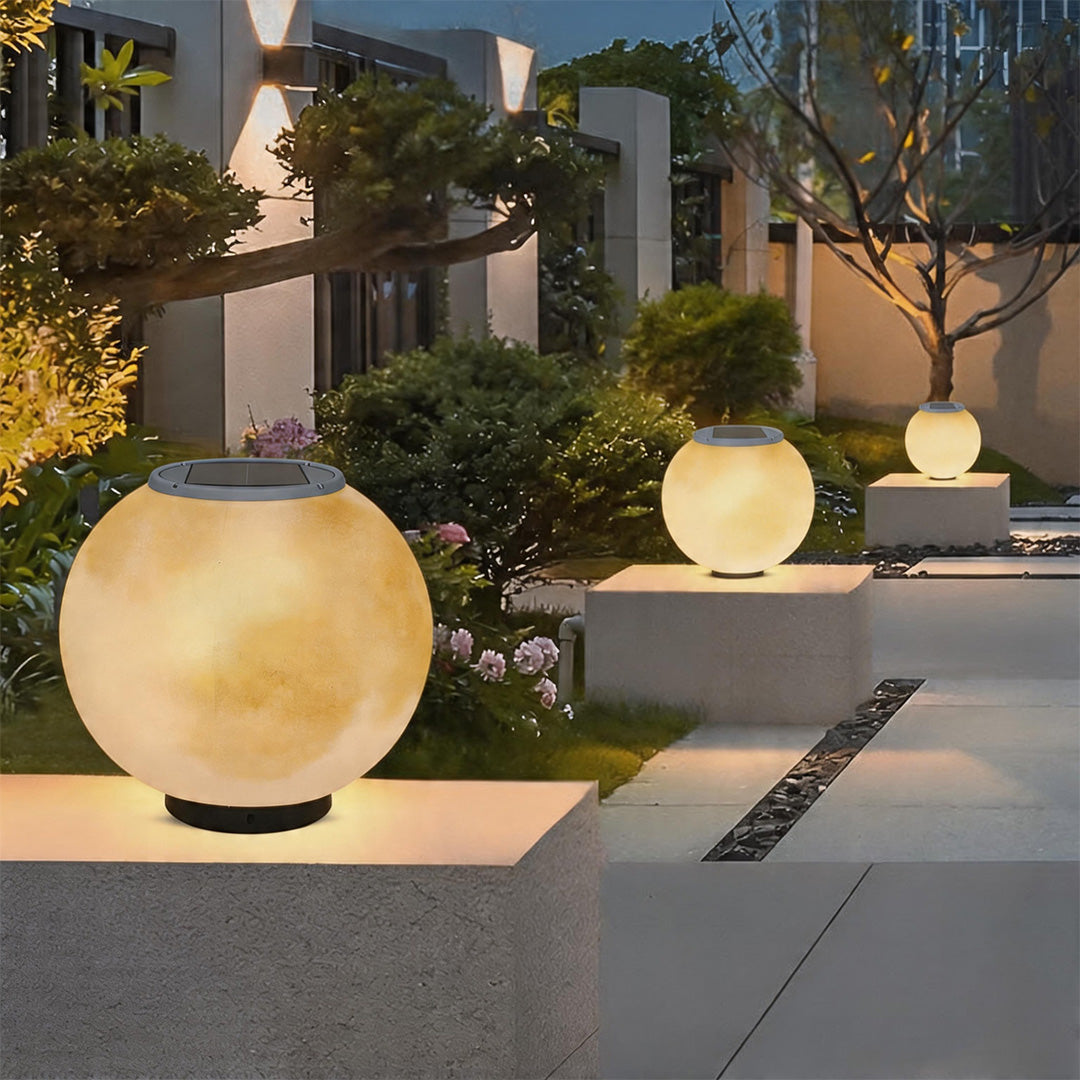 Solar powered moon pillar lights with top panels glowing on concrete posts in a modern garden.