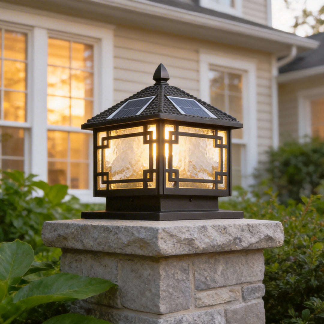 Solar powered outdoor garden pillar lights illuminating a granite fence post near a home window.