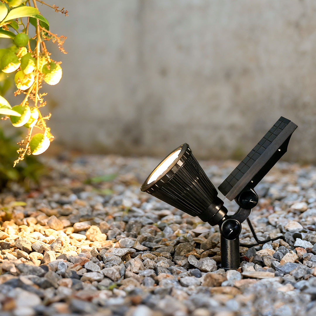 Solar powered spotlights illuminating garden gravel, adjustable black spotlight head designed for outdoor landscape lighting at night.