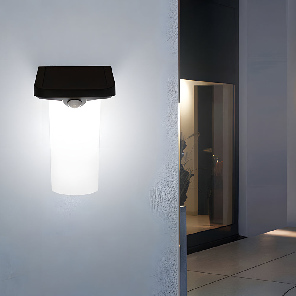 Solar wall lamp with motion sensor illuminating a pathway beside a house.
