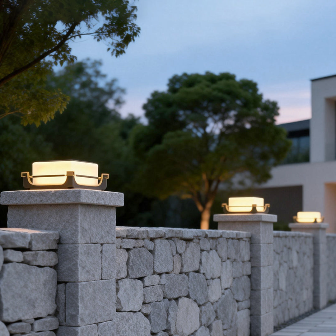 Square acrylic pier light mounted on stone fence pillars, providing warm accent lighting for a modern villa exterior.