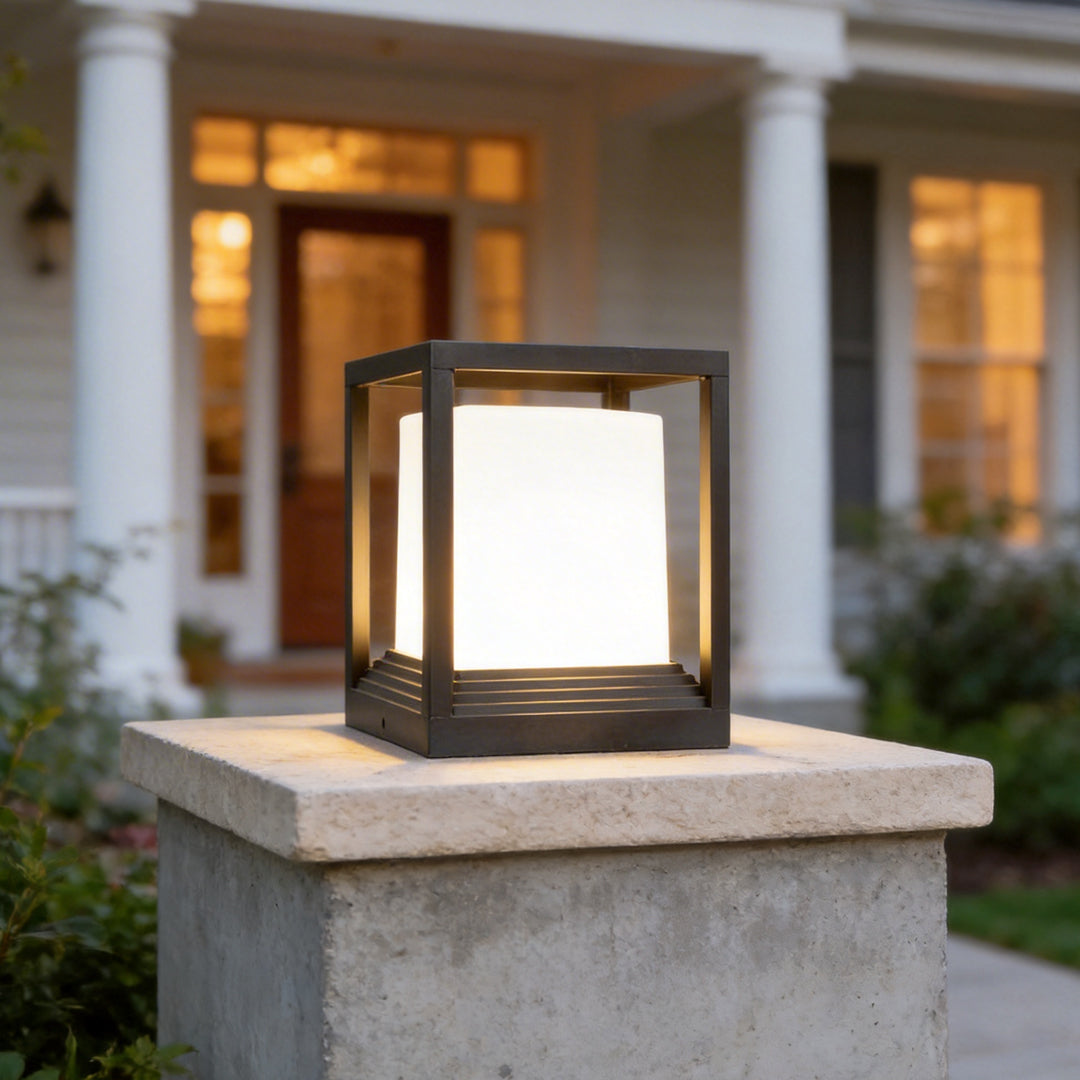 Square black garden pedestal lights with a warm glow mounted on a concrete pillar at daytime.