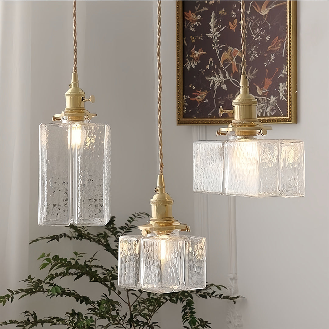 Square glass pendant light in cozy bedroom setting with textured bedding and warm neutral color palette.