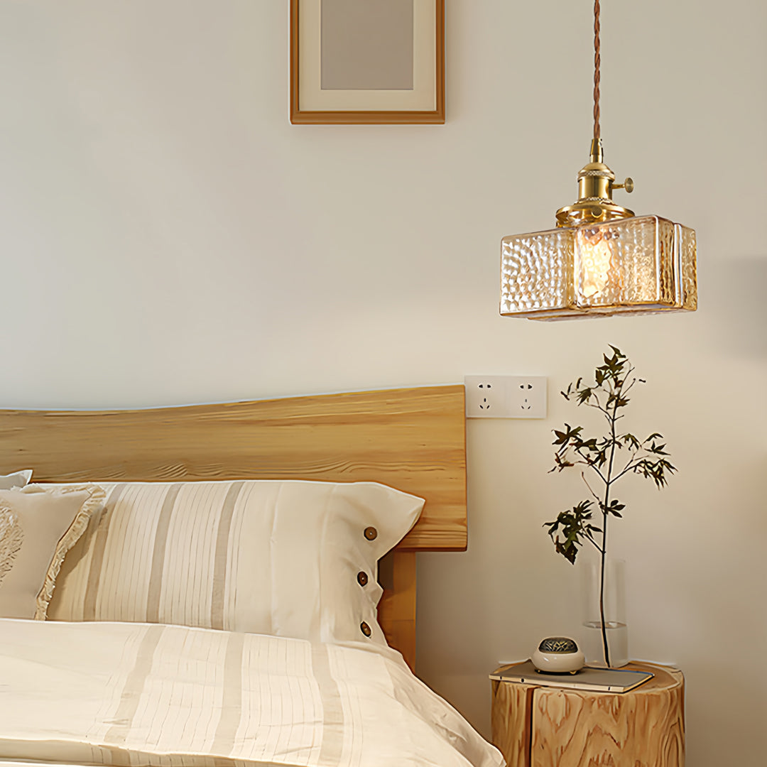 Square glass pendant light illuminating contemporary kitchen island with warm brass accents and neutral tones.