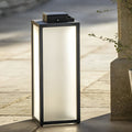 Square handheld lantern with sleek black frame beside tree in garden.