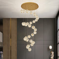 Spiral staircase crystal chandelier installed in a tall modern staircase area.