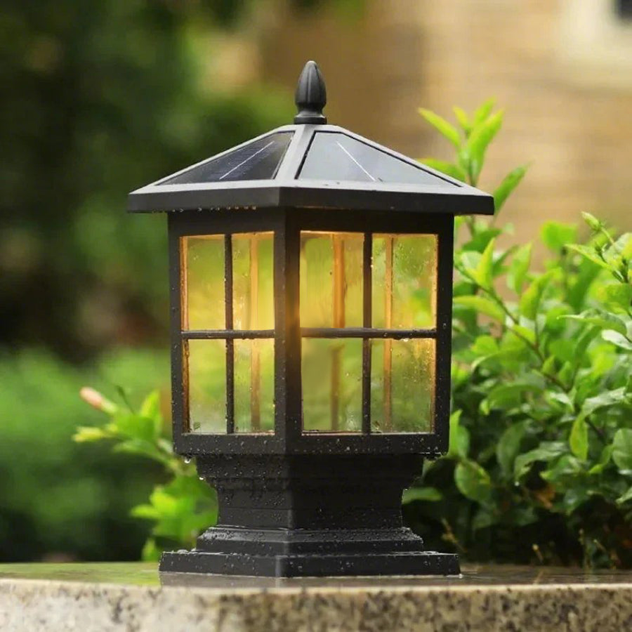 Stone light pillar with a black lantern, illuminating a pathway surrounded by greenery.
