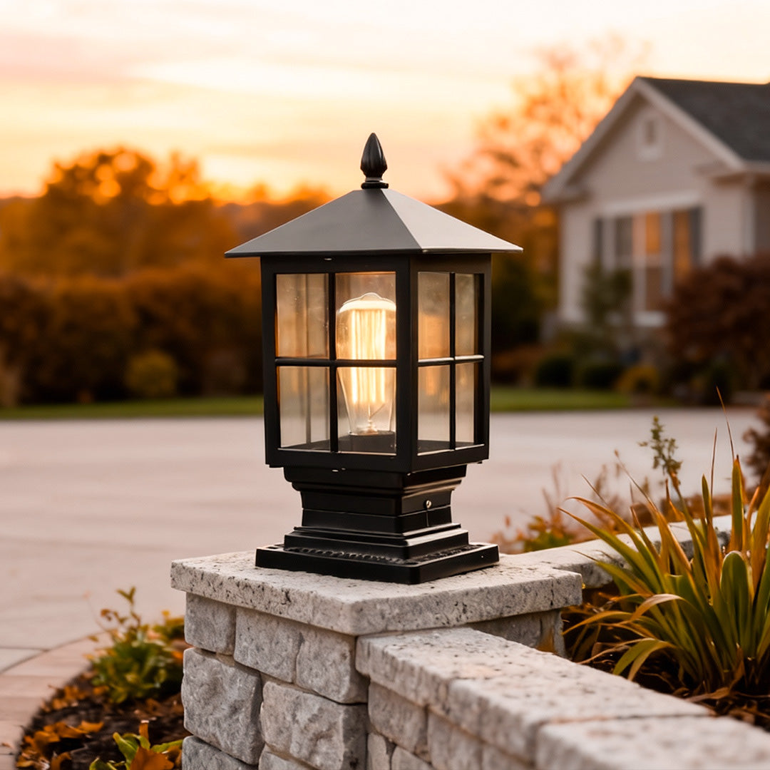 Stone light pillar with a classic black lantern, providing warm illumination near a driveway entrance.