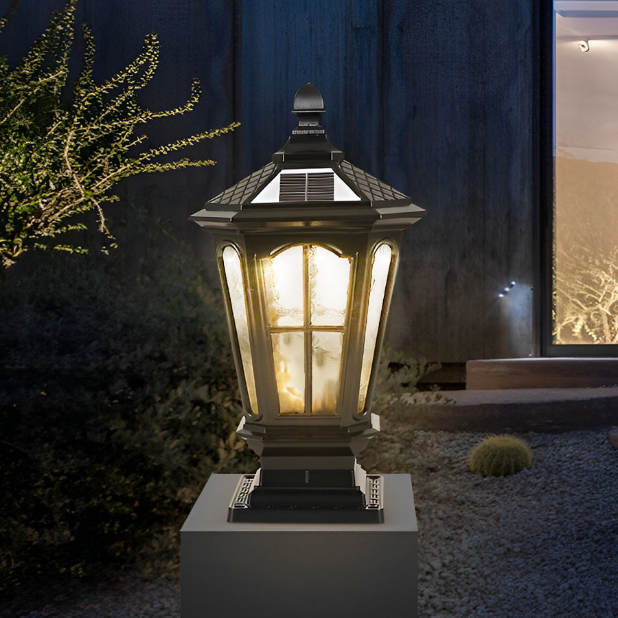 Traditional black stone pillar light fixture with warm glow mounted on square stone base in garden setting.