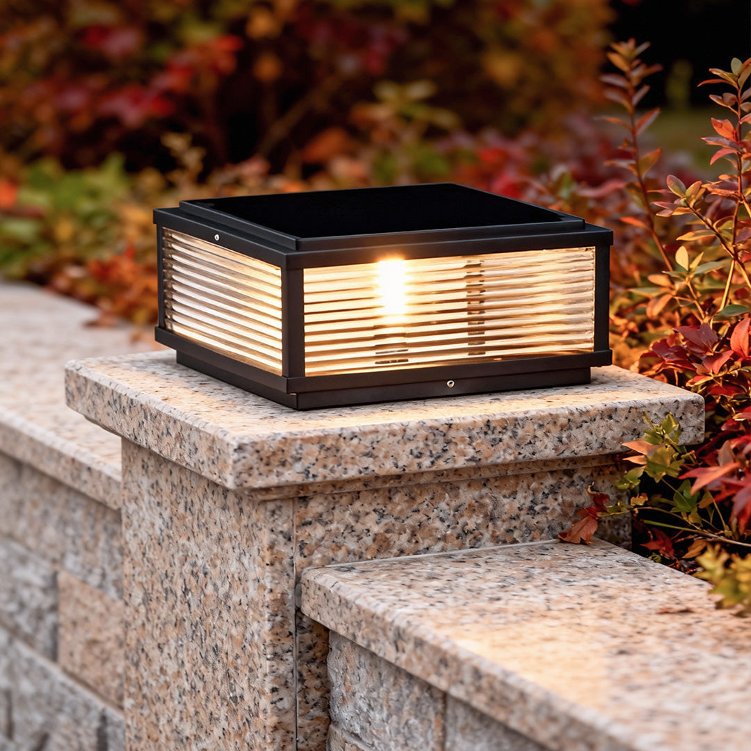 Square pillar light installed on stone pillar beside colorful shrubs, providing stylish garden illumination.