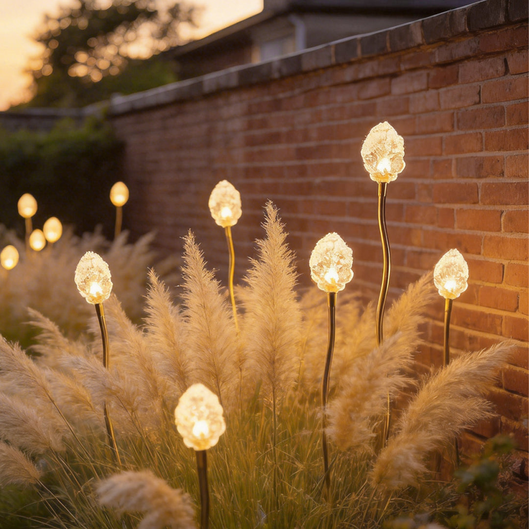Syphasera standing lamp installed along a brick wall landscape creating warm ambient garden lighting.