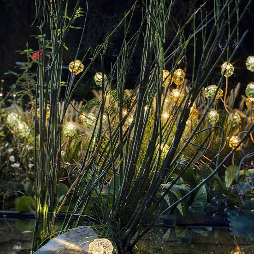 Syphasera standing lamp illuminating tall reeds and water features in a serene garden setting.