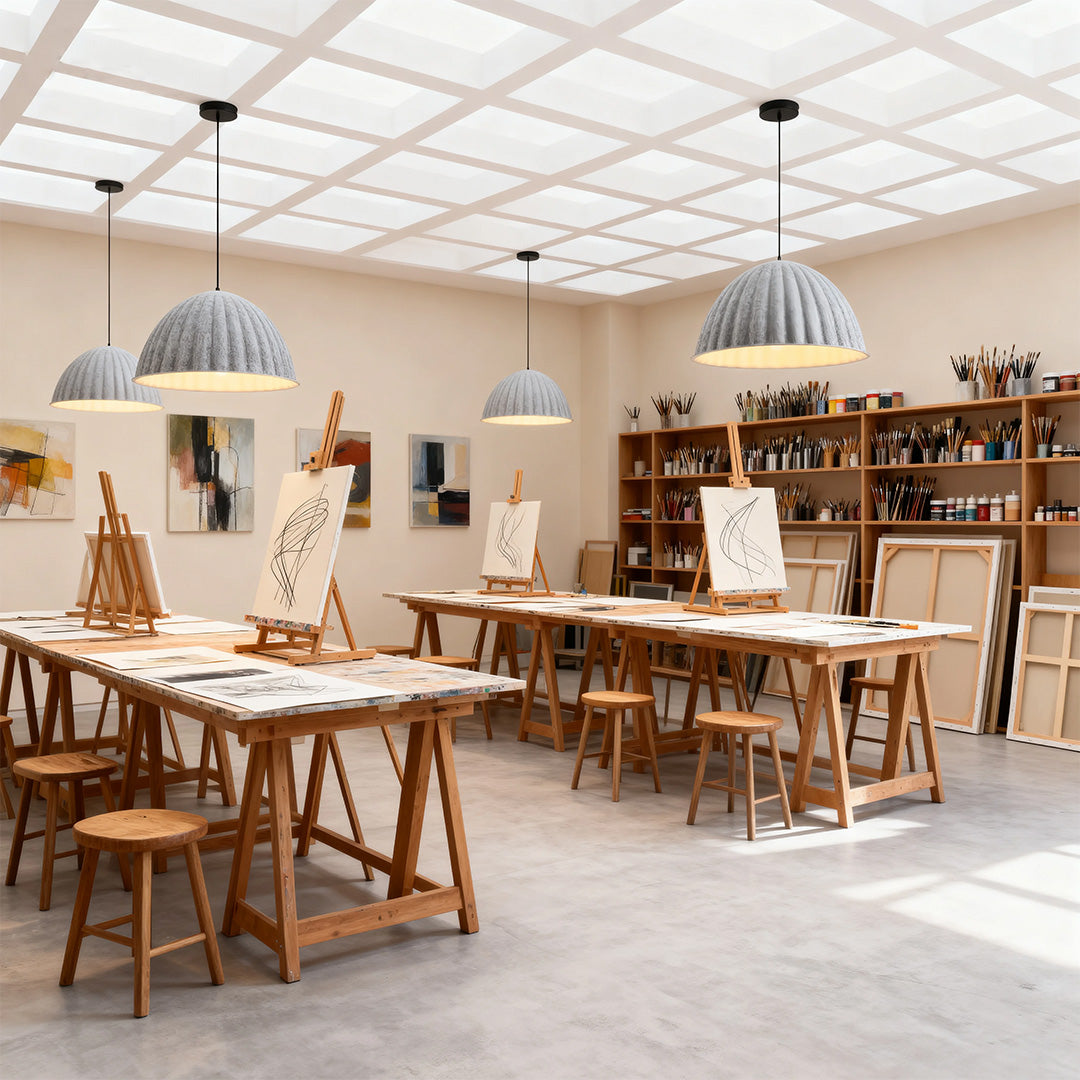 Multiple textured gray pendant light fixtures providing overhead illumination in a bright, organized art classroom studio.