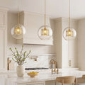 Trio of Clear Glass Globe Pendant lights with brass mesh interiors over a marble kitchen island.