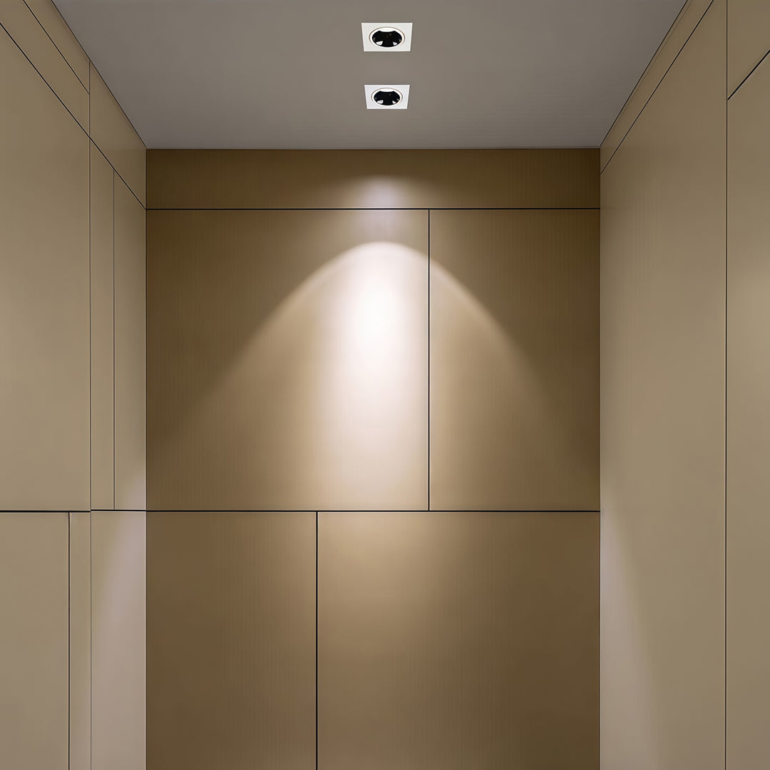 Two square recessed downlight fixtures creating a focused wall-wash effect on a beige paneled wall.