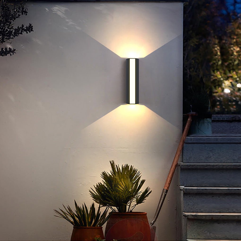 Minimalist up down cylinder sconce casting sharp light patterns on a smooth wall, ideal for modern outdoor stairway lighting.