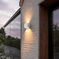 Up and down wall lights illuminating a modern house facade with warm directional glow.