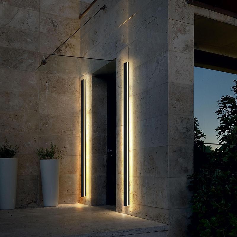 Vertical linear outdoor wall sconce with warm light, enhancing the entrance of a modern residential building.